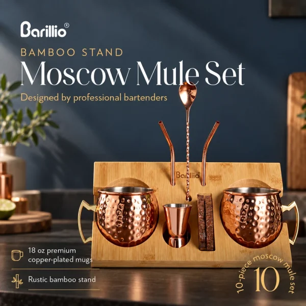 Two hammered copper-colored Moscow Mule mugs on a bamboo stand with a jigger, bar spoon and bent straws